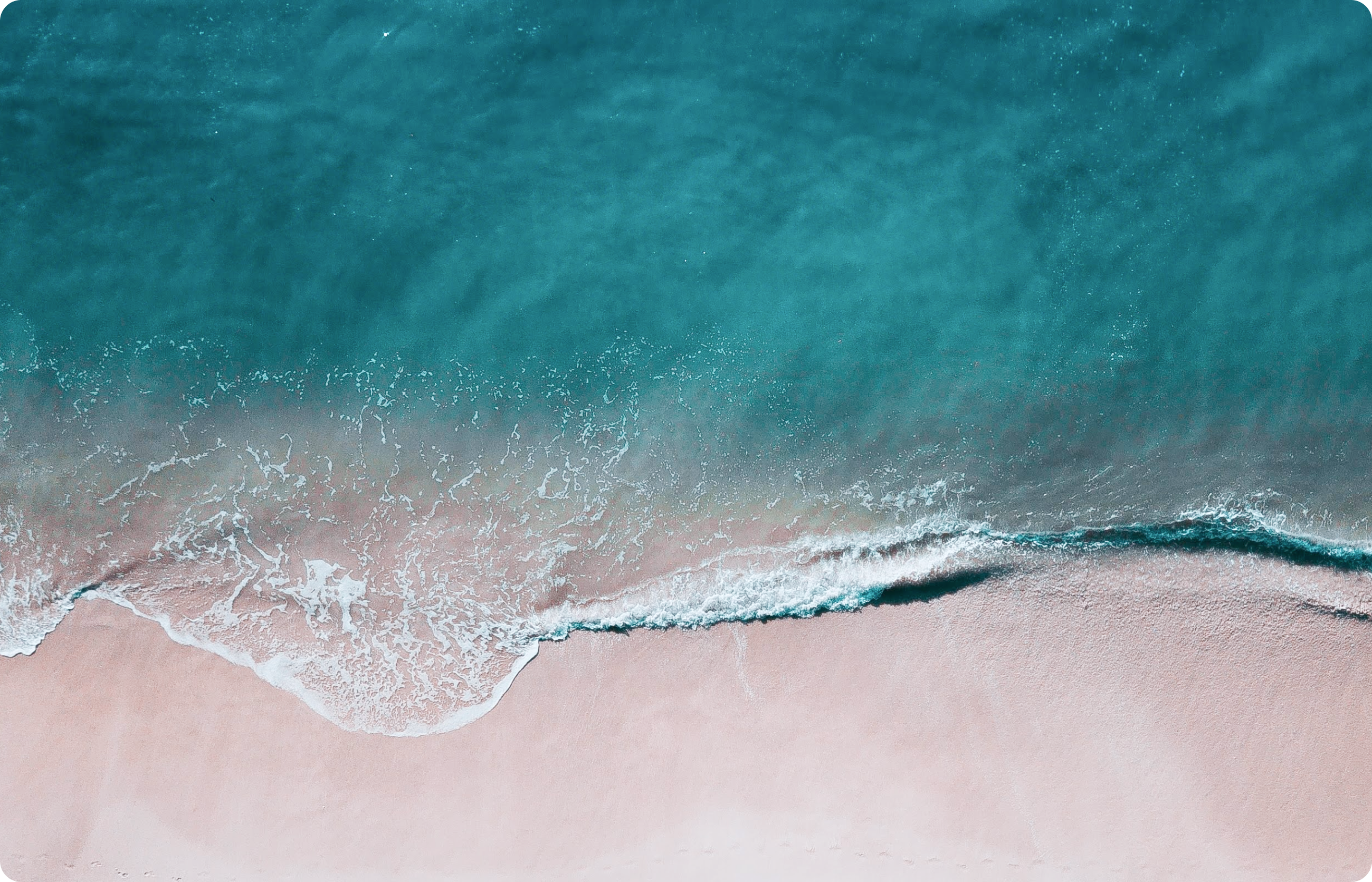 空撮で捉えられた海岸線で、透き通る青い海が砂浜に波打ち寄せている様子