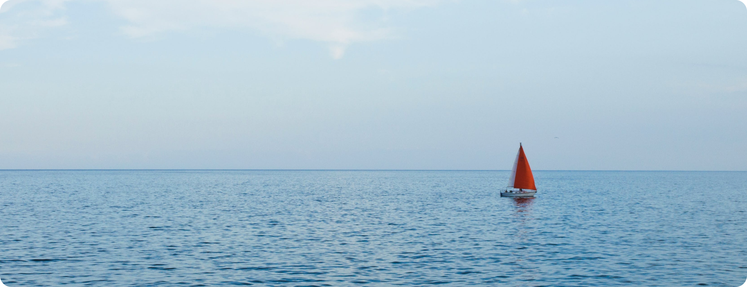 静かな海に浮かぶ、赤い帆を持つヨットが一隻、遠くに見える
